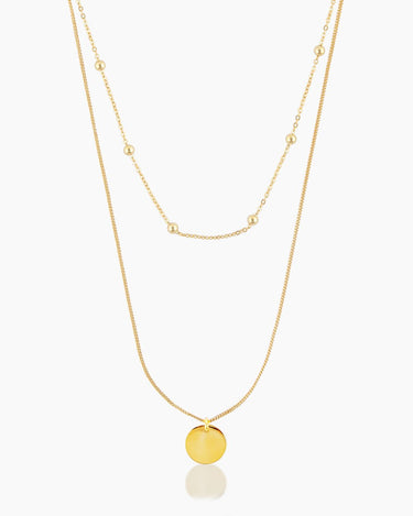 The Lucia Necklace, a gold beaded choker layered with a golden pendant