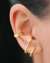 A gold illusion earring and a gold illusion ear cuff that look like two earrings and two cuffs