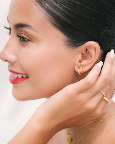 A woman wearing a gold illusion earring that looks like two earrings, gold rings, and necklaces