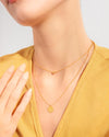 A close up shot of a woman wearing the Sofia Necklace, a gold two-layer illusion necklace with a dainty golden ball and a classic round pendant