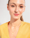 A woman wearing the Sofia Necklace, a gold two-layer illusion necklace with a dainty golden ball and a classic round pendant