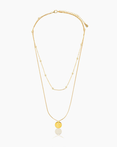 The Lucia Necklace, a gold beaded choker layered with a golden pendant