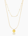 The Lucia Necklace, a gold beaded choker layered with a golden pendant