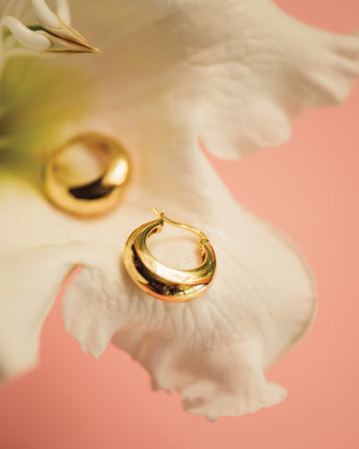 The Hailey Hoops, chunky yet elegant gold hoop earrings, on a flower background