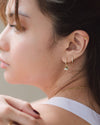 A woman wearing the Amelie Huggies, a butterfly dangler earring, a butterfly ear cuff, and a gold necklace
