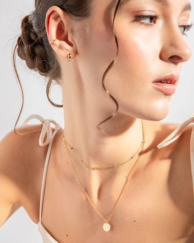 A woman wearing the Lucia Necklace, a gold huggie earring, and a gold ear cuff