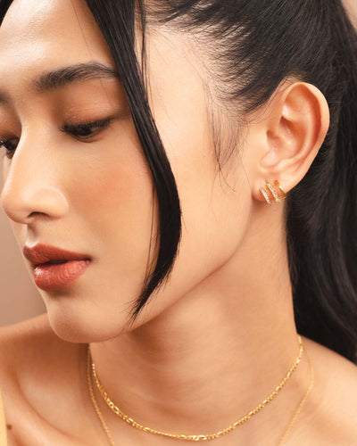 A woman wearing a triple-stacked gold illusion earring, a gold choker necklace, and another gold necklace