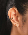 A close up shot of an ear wearing the Darla Cuffs and the Brooke Huggies, double stacked gold illusion earrings featuring both round cut and baguette cut cubic zirconia