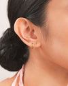 A woman wearing the Emilia Huggies, gold double-stacked illusion earrings featuring one hoop paved with cubic zirconia