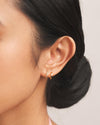 A close up shot of the left ear of a woman wearing the Emilia Huggies, gold double-stacked illusion earrings featuring one hoop paved with cubic zirconia
