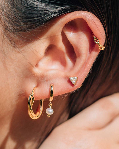 A close up shot of the Twilly Hoops, Mara Cuffs, Arielle Huggies, and Trinity Pearl Studs worn on a woman's ear