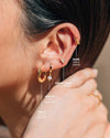 A labeled photo of the Twilly Hoops, Mara Cuffs, Arielle Huggies, and Trinity Pearl Studs worn on a woman's ear